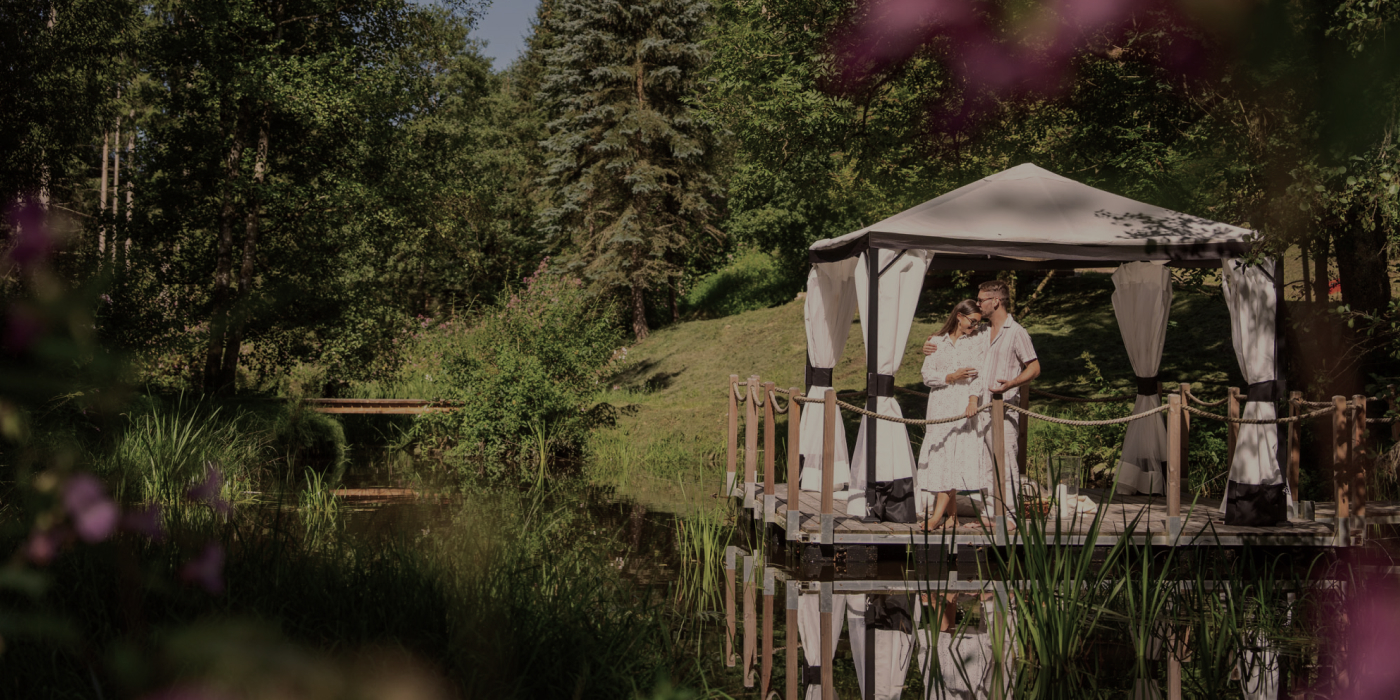 Forstgut Chalet Bayerischer Wald – Pärchen genießt romantischen Urlaub zu zweit am See mit Pavillon in Bayern.